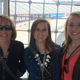 Three women who like cars, at the race track, watching cars.
